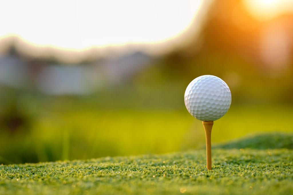 Golftee mit Ball auf dem Grün im Gegenlicht